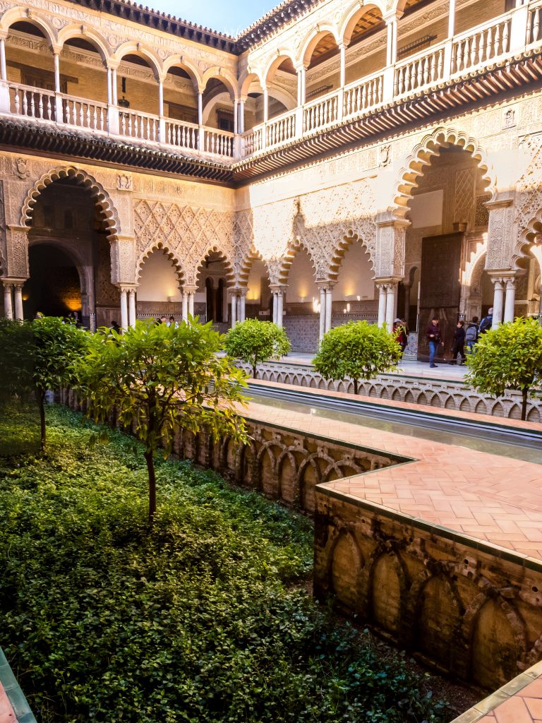 The Courtyard of the Maidens in the Alcazar of Seville with a water feature and small trees